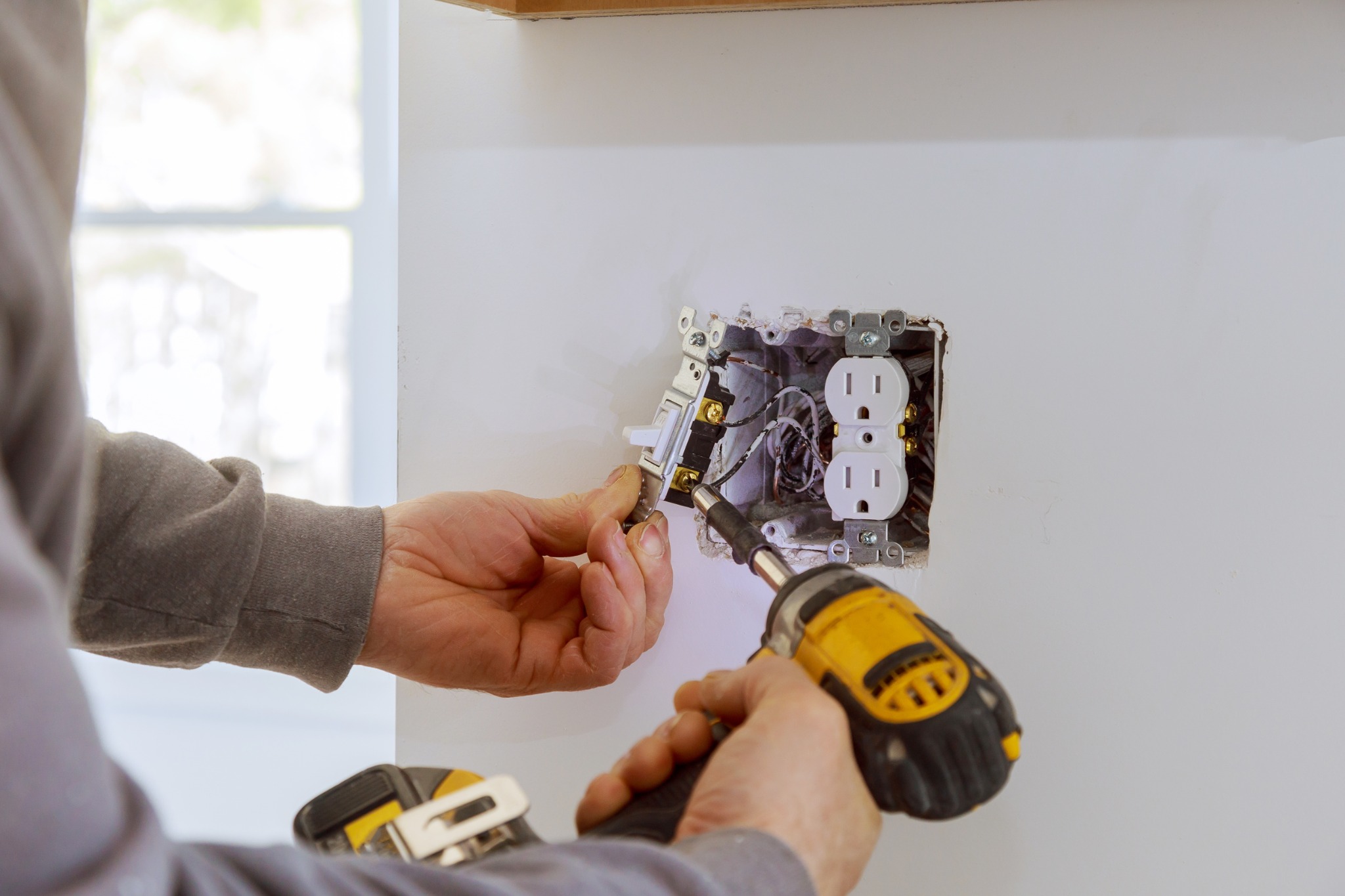 Electrician installing white duplex outlet with drill and gloved hands