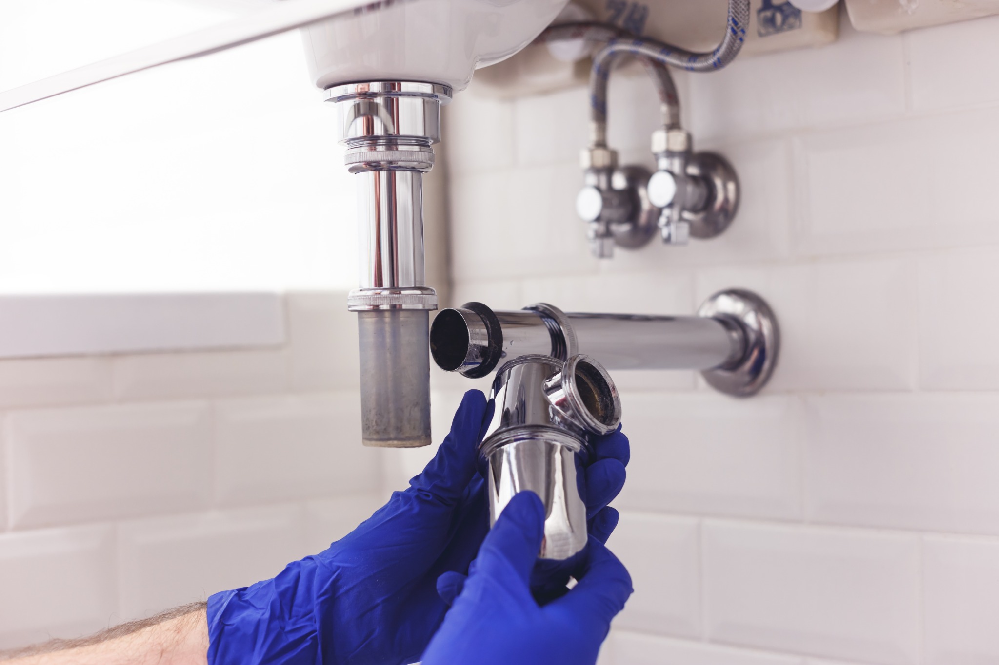 Plumber in blue gloves installing chrome P-trap under bathroom sink