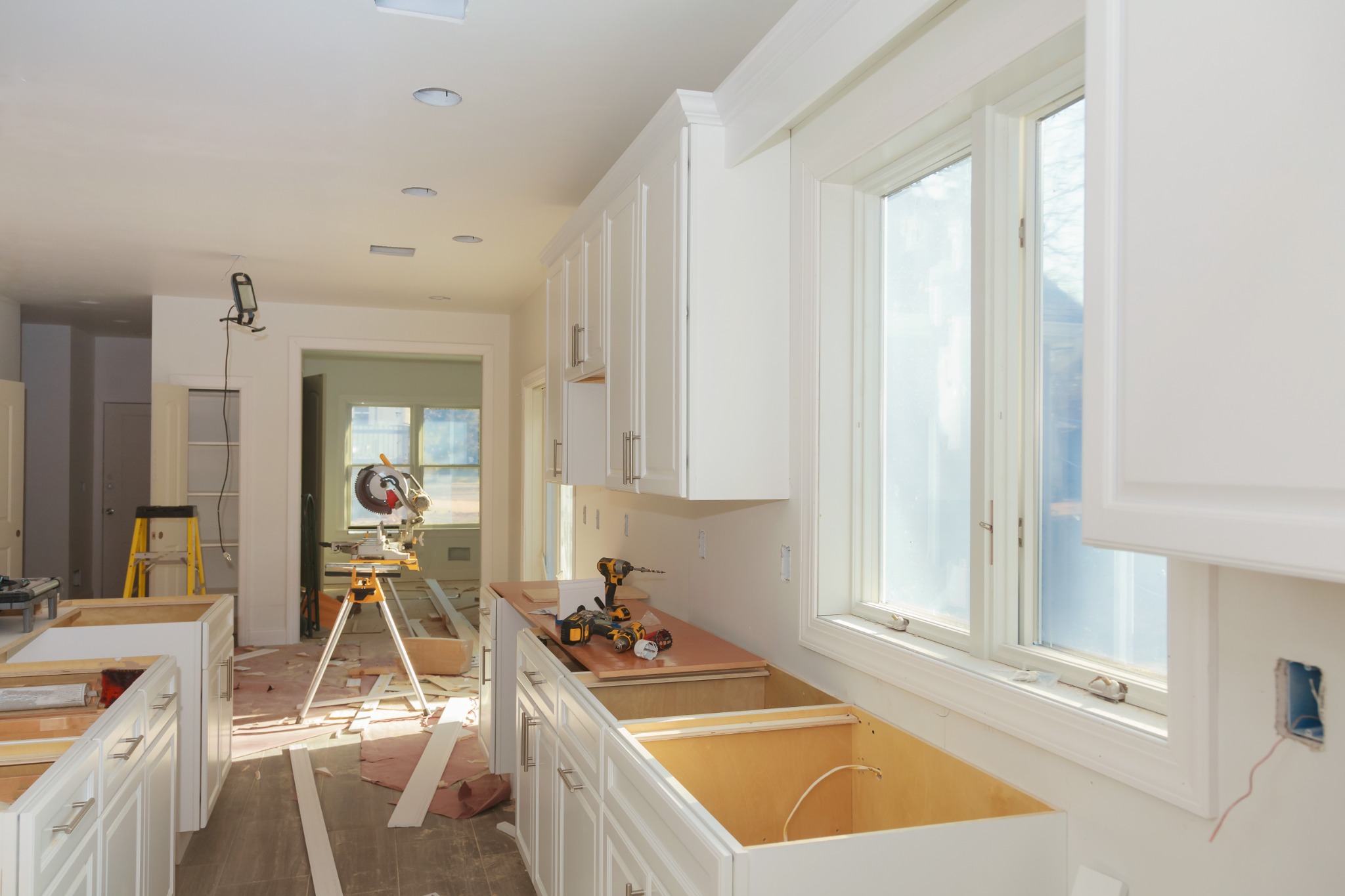 Kitchen under renovation with white cabinets, power tools, and construction equipment visible